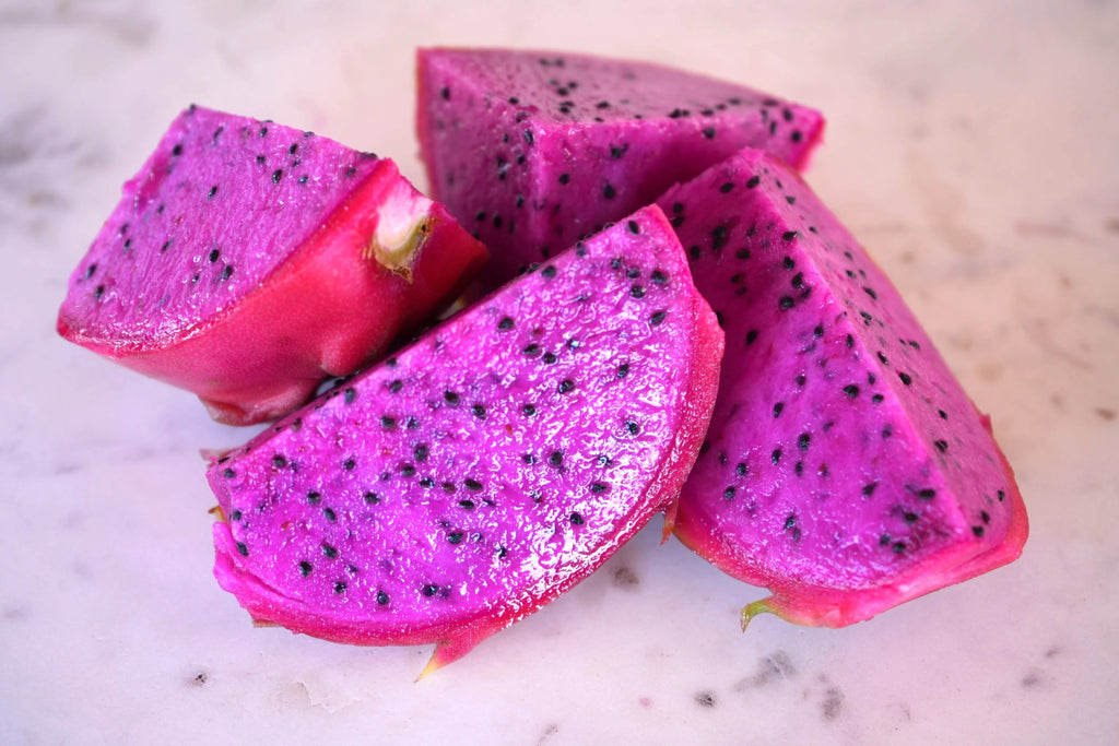 Fresh sliced purple dragon fruit with black seeds on a marble surface